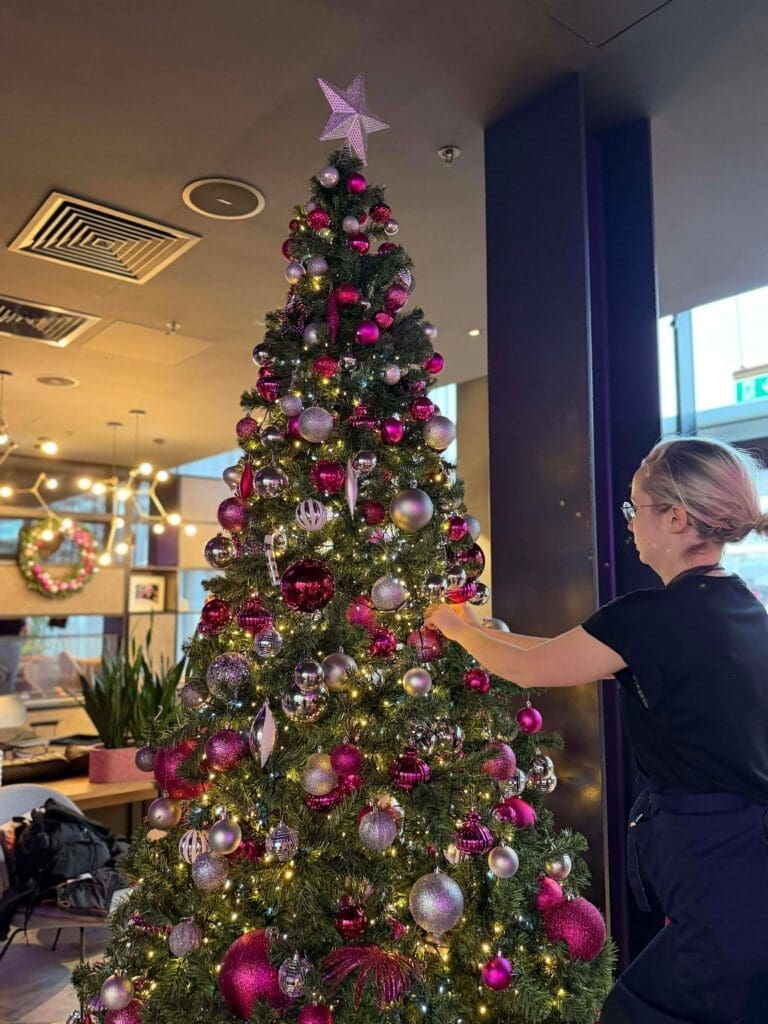 Team member decorating a Christmas tree in a venue lobby